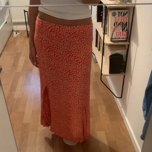 Röd blommig långkjol från MNG - Säljer en superfin röd långkjol från Mango med ett sött blommigt mönster i vitt. Kjolen har knappar på sidan och en diskret dragkedja i bak. 