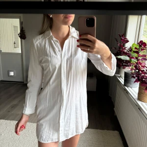 Skjortklänning från Asos i storlek 36 - Vit skjortklänning från Asos i storlek 36. Enstaka fläck förekommer (se bild) men inget som syns tydligt. Dolda knappar framtill och knappar i ärmslut. Min längd 174 cm.