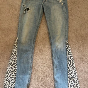 Lågmidjade bootcut jeans - Unika jeans från Hollister med leopardmönster vid bensluten. De har en sliten look med revor på framsidan och klassisk femficksdesign. Bra skick
