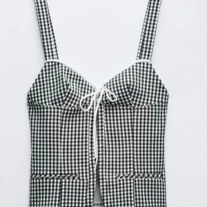 Zara topp - Snygg svartvit rutig korsett med breda axelband och dragkedja bak. Den har en knytning framtill som ger en fin detalj. Perfekt för att ge en stilren look med en touch av retro.