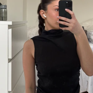 Svart ärmlös polotopp - Snygg svart ärmlös polotopp som passar perfekt för en stilren look. Toppen har en hög krage och är tillverkad i ett mjukt material som ger en bekväm passform.