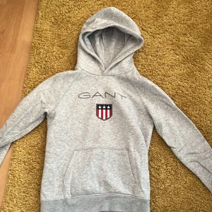 Grå hoodie från GANT - Säljer en stilren grå hoodie från GANT med broderad logga och ett emblem. Pris kan diskuteras 