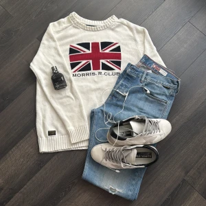 Vit tröja från Morris R. Club - Säljer en stilren vit tröja från Morris R. Club med ett stort Union Jack-motiv på framsidan. Tröjan har långa ärmar och ribbade muddar vid ärmslut och nederkant. Perfekt för en avslappnad och trendig look.