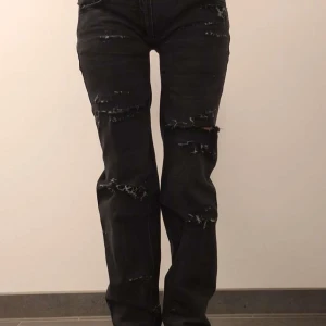 Svarta slitna jeans - Snygga svarta jeans med slitningar på framsidan och bakfickorna. De har en klassisk femficksdesign och en modern look med slitna detaljer. Perfekta för en avslappnad stil.