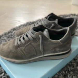 Grå sneakers från Philippe Model - Snygga grå sneakers från Philippe Model i mocka. Skorna har en klassisk design med snörning och en bekväm sula. Perfekta för en stilren look.