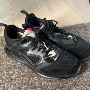 Svarta Nike Air Max 720 - Säljer ett par svarta Nike Air Max 720 med en futuristisk design och synlig Air-enhet i sulan. Skorna har en kombination av mesh och syntetmaterial för ökad komfort och hållbarhet. De har snörning och en röd detalj på sulan.