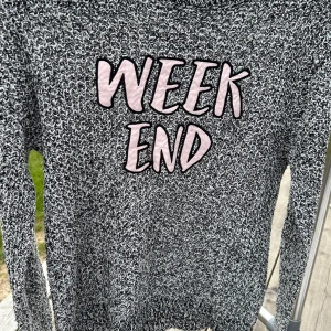 Svartvit stickad tröja från FB Sister - Säljer en svartvit stickad tröja från FB Sister med texten 'WEEKEND' i rosa på framsidan. Tröjan har långa ärmar och en mysig känsla, perfekt för avslappnade dagar. På baksidan är det ingen text eller något annat mönster.