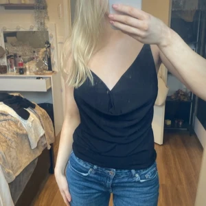 Svart  topp - Säljer en stilren svart ärmlös topp med smala axelband och v-ringning. Perfekt för en enkel och elegant look. Passar bra till jeans eller kjol.