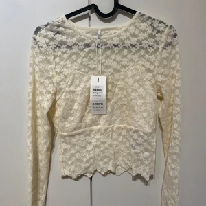Vit spetsblus från ONLY - Säljer en vit spetsblus från ONLY med långärmad design. Blusen har ett blommigt mönster och är croppad. Original pris 259, prislappen sitter fortfarande på så helt ny.