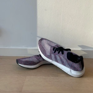 Nike Flyknit sneakers i flerfärgad design - Snygga Nike Flyknit sneakers med en flerfärgad design i rosa, blått och vitt. Skorna har en lätt och flexibel Flyknit-ovandel med svarta snören och en vit sula. Perfekta för en sportig och stilren look.