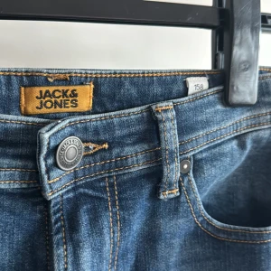 Blå jeans från Jack & Jones - Snygga blå jeans från Jack & Jones i slim fit-modell. De har en klassisk femficksdesign med knapp och dragkedja framtill. Perfekta för en stilren look. Stl 156