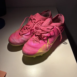Rosa Nike fotbollsskor med Zoom-teknologi - Säljer mina gamla fotbollsskor. De är använda länge och därmed slitits (se bilder). De funkar bra fortfarande. Hålen på sidan går inte igenom, bara slitet på utsidan 