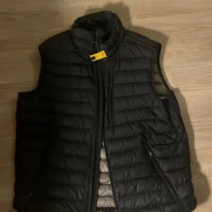 Svart dunväst från Parajumpers - Säljer en svart dunväst från Parajumpers med dragkedja och en gul detalj vid halsen. Västen har en quiltad design och flera praktiska fickor. Perfekt för kyligare dagar äkta hets bevis medföljer säljer då den jag växt ur den.