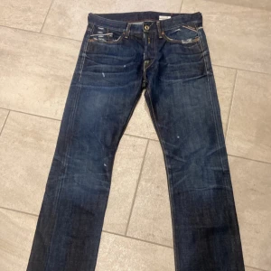 Mörkblå jeans från Replay - Snygga mörkblå jeans från Replay med slitna detaljer och klassisk femficksdesign. De har en knappgylf och kontrastsömmar som ger en cool look. Perfekta för en avslappnad stil. Storleken är w30/34