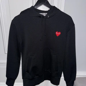 Svart hoodie från Comme des Garçons - Säljer en stilren svart hoodie från Comme des Garçons med det ikoniska röda hjärtat på bröstet. | Skick: 10/10 | Nypris: 2349kr | Vårt pris: 999kr | Tveka inte att höra av dig vid minsta fråga! Mvh