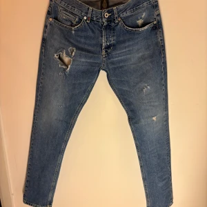 Dondup George jeans blå - Snygga blå jeans från Dondup George med slitna detaljer och en klassisk femficksdesign. Tillverkade i Italien med en blandning av bomull och polyester för en bekväm passform. Perfekta för en avslappnad stil. Passar längden mellan 180-190 cm vikt spelar ingen roll toppen skick utan defekter.