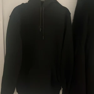 Svart hoodie från Hugo Boss - Säljer en stilren svart hoodie från Hugo Boss. Den har en klassisk design med dragsko i huvan och en diskret logga på bröstet. Perfekt för en avslappnad och trendig look.