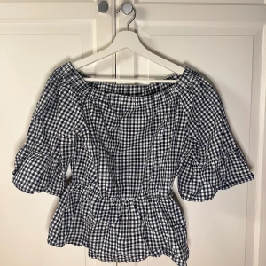 Rutig blus från Gina Tricot - Säljer en söt rutig blus från Gina Tricot i svart och vitt. Blusen har trekvartsärmar och en elastisk midja som ger en fin passform. Perfekt för en avslappnad stil. Tillverkad i 100% bomull.