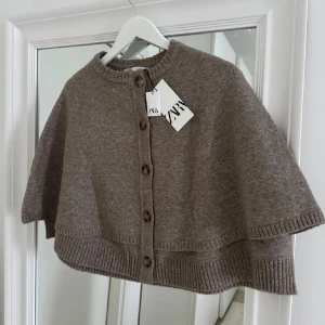 Beige cape från Zara - Säljer en stilren beige cape från Zara med knappar framtill. Perfekt för lager-på-lager under höst och vår. Den är stickad och har en mjuk och bekväm känsla. Ett snyggt tillskott till garderoben! Jag hade även kunnat tänka mig att byta till en storlek S. (bilderna är lånade från förra säljaren). Bilderna är lånade, så prislappen är ej kvar men den är i ett mycket mycket bra skick. 