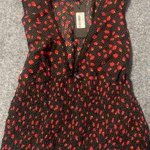 Svart topp med röda prickar - Trendig svart topp  med röda prickar och v-ringad design. Perfekt för en färgglad look. Klänningen har en smickrande passform och är tillverkad i ett lätt material.