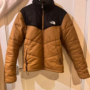 North Face Puffer Jacka - Köpt begagnad, endast använd förra vintern av mig, har några fläckar men syns inte särskilt mycket (fråga om fler bilder om det behövs), en plupp på dragkedjan där nere är av (se sista bild) men funkar oftast som den ska