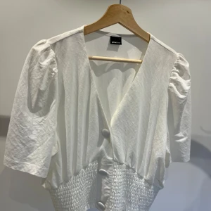 Vit blus från Gina Tricot - Säljer en superfin vit blus från Gina Tricot i storlek L. Den har en v-ringad design med knappar framtill och puffiga trekvartsärmar. Blusen är gjord i ett mjukt och bekvämt material, perfekt för både vardag och fest!