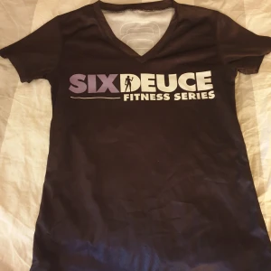Svart t-shirt från Six Deuce - Säljer en ny svart t-shirt från Six Deuce med tryck på framsidan i lila och vitt. Den har en v-ringad hals och korta ärmar, perfekt för träning eller vardagsbruk. Materialet känns mjukt och luftigt. Passar bra för dig som gillar en sportig stil! 