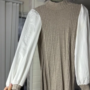 Beige ribbad klänning med vita ärmar - Säljer en superfin beige ribbad klänning med långa vita puff ärmar. Klänningen är tight och perfekt för höst och vår. Den har en stilren design med en hög krage och är tillverkad i ett mjukt material som är super mysig🤎🤍