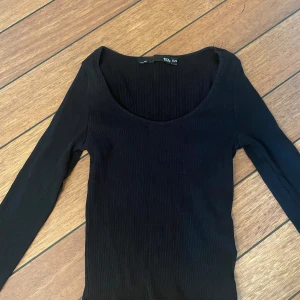 Svart ribbad topp från 157 - Säljer en stilren svart ribbad topp från 157 i storlek XS. Den har en djup rundad hals och långa ärmar. Toppen är i bra skick och passar till alla säsonger. Skön och stretchig, så den sitter snyggt på kroppen. Passar även S 
