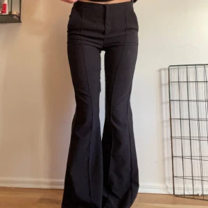 Svarta bootcut byxor - Säljer ett par snygga svarta kostymbyxor som sitter perfekt för både vardag och fest. De är högmidjade och har en stilren dragkedja design med  och knapp framtill. Materialet är mjukt och stretchigt, vilket gör dem superbekväma att ha på sig. ❤️ 