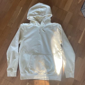 Vit hoodie från Colorful Standard - Säljer en supermjuk och bekväm vit hoodie från Colorful Standard. Den är gjord av ekologisk bomull och är förtvättad för extra komfort. Perfekt för alla årstider och har en klassisk passform med en stor ficka fram och justerbar huva. Tillverkad i Portugal.