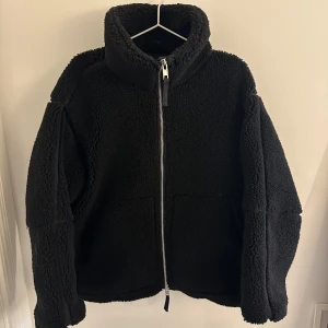 Svart teddyjacka med dragkedja - Säljer en supermysig svart teddyjacka i storlek S. Den har en hög krage och en dragkedja framtill. Perfekt för kyliga höst- och vinterdagar när du vill hålla dig varm och stilren. Jackan är i toppen skick och redo för nya äventyr!