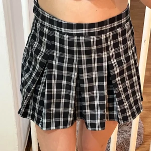Svart och vit rutig kjol - Säljer en superfin svart och vit rutig kjol med veckad design. Den är perfekt för både vardag och fest! Kjolen har en hög midja och är i kort modell, vilket ger en snygg och trendig look. Passar perfekt till en enkel topp eller en stickad tröja för kyligare dagar.