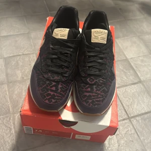 Nike Air Max 1 CMFT PRM Tape - Säljer ett par snygga Nike Air Max 1 CMFT PRM Tape sneakers i svart med coola mönster i rosa och beige detaljer. Skorna har en klassisk Air Max-sula för extra komfort och stil. Perfekta för både vardag och fest!