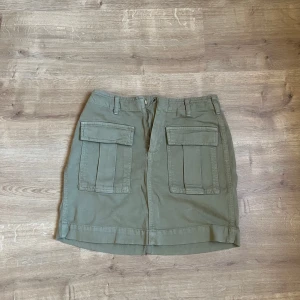 Grön kjol med fickor - Snygg grön kjol med stora fickor framtill och bälteshällor. Perfekt för en avslappnad stil. Kjolen har en rak passform och är knälång.