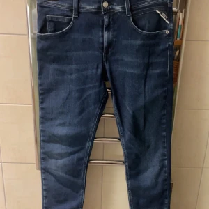 Mörkblå jeans från Replay - Snygga mörkblå jeans från Replay med klassisk femficksdesign och knappgylf. Perfekta för en stilren look. Märkesdetalj vid fickan ger en extra touch.