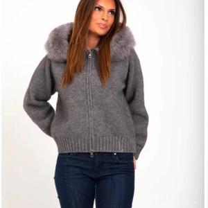 Grå stickad jacka med pälskrage - Säljer en mysig grå stickad jacka med en fluffig pälskrage. Jackan har dragkedja framtill och ribbade muddar vid ärmslut och nederkant. Perfekt för kyliga dagar!