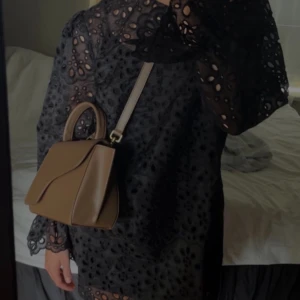 Svart spetsklänning hm - Säljer en elegant svart spetsklänning med långärmad design och vackra broderade detaljer. Klänningen har en luftig passform och är perfekt för en stilfull look. Den har en rund hals och fina volanger vid ärmsluten.