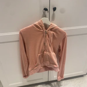 Rosa hoodie från Juicy Couture - Säljer en snygg rosa hoodie från Juicy Couture. Den har en dragkedja framtill och en praktisk ficka. Perfekt för en avslappnad stil med sin mjuka och bekväma design.