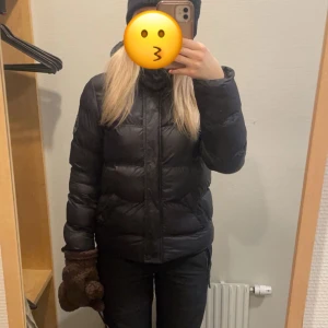 Svart dunjacka - Säljer en svart dunjacka som är perfekt för kalla dagar. Jackan har en pufferdesign med långa ärmar och en hög krage för extra värme. Den är stilren och enkel att matcha med olika outfits.