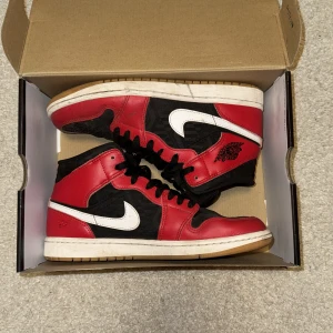 Nike Air Jordans i rött och svart - Snygga Nike Air Jordans i klassisk röd och svart färgkombination med vit sula. Skorna har en ikonisk design med snörning och Nike-logga på sidan. Perfekta för dig som vill ha en stilren och sportig look.