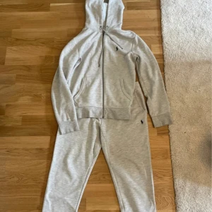 Grå hoodie från Ralph Lauren - Säljer en stilren grå hoodie från Ralph Lauren med dragkedja och huva. Tröjan har långa ärmar och en liten broderad logotyp på bröstet. Perfekt för en avslappnad look.