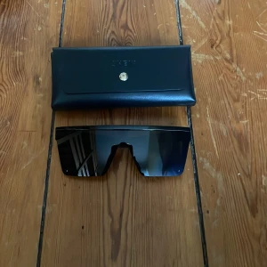 Svarta solglasögon med fodral - Snygga svarta solglasögon med en modern, kantig design. De har en bred, hel lins som ger ett futuristiskt intryck. Kommer med ett stilrent svart fodral för säker förvaring. Pris går att diskuteras 