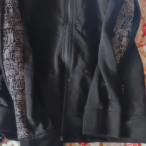 Svart jacka från Hugo Boss - Snygg svart jacka från Hugo Boss med dragkedja och unikt mönster längs ärmarna. Perfekt för en stilren look. Jackan har långa ärmar och en bekväm passform.