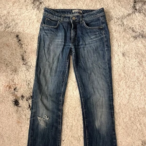 Acne jeans - Retro jeans från Acne Jeans i strl 28/32 i rak modell med liten slitning vid ena knäet. Ej skinny elr bootcut, utan sitter tight vid låren och svänger ut längs med vaderna. Passar mig som är 163 lång och vanligtvis S i byxor 🩵Har ett hål som går att laga (se bild)