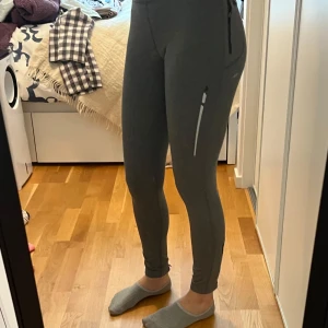 Grå tights med ficka - Snygga grå tights med ficka på sidan. Perfekta för träning eller en avslappnad dag. De har en tight passform och är tillverkade i ett stretchigt material och har även dragkedjor på sidorna längst ner på dem. 