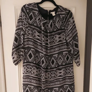Svartvit mönstrad klänning - Säljer en svartvit klänning med geometriskt mönster. Klänningen har trekvartsärmar och en rund halsringning. Perfekt för en stilren look.