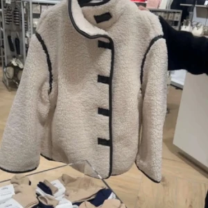 teddyjacka - INTRESSEKOLL på en mysig teddyjacka med mörkbruna/ svarta kantdetaljer och knappar. Jackan har en hög krage och långa ärmar, perfekt för kyliga dagar. Den är både stilren och bekväm, ett måste i garderoben!