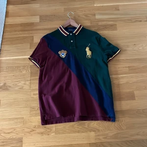 Flerfärgad pikétröja från Polo Ralph Lauren - Snygg pikétröja med diagonala block i vinrött, grönt och blått. Tröjan har en broderad logga på bröstet och en krage med knappar. Perfekt för en stilren look.