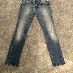 Blå jeans från Replay - Snygga blå jeans från Replay med en klassisk femficksdesign och coola detaljer som metallknappar och nitar. Jeansen har en lätt tvättad look en normal passform som passar perfekt till vardags. En defekt som visas på sista bilden, vid fler frågor eller bilder är det bara att skriva 